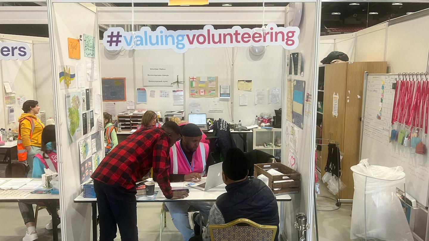 Voluntarios en un stand de exposición hablando sobre trabajo en una laptop.